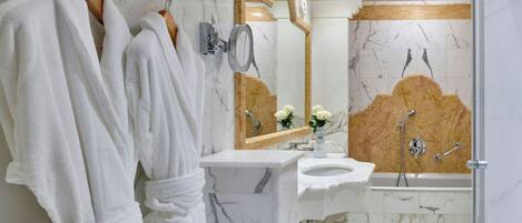 A bathroom with marble walls, a sink, a mirror, and two white robes hanging on hooks.