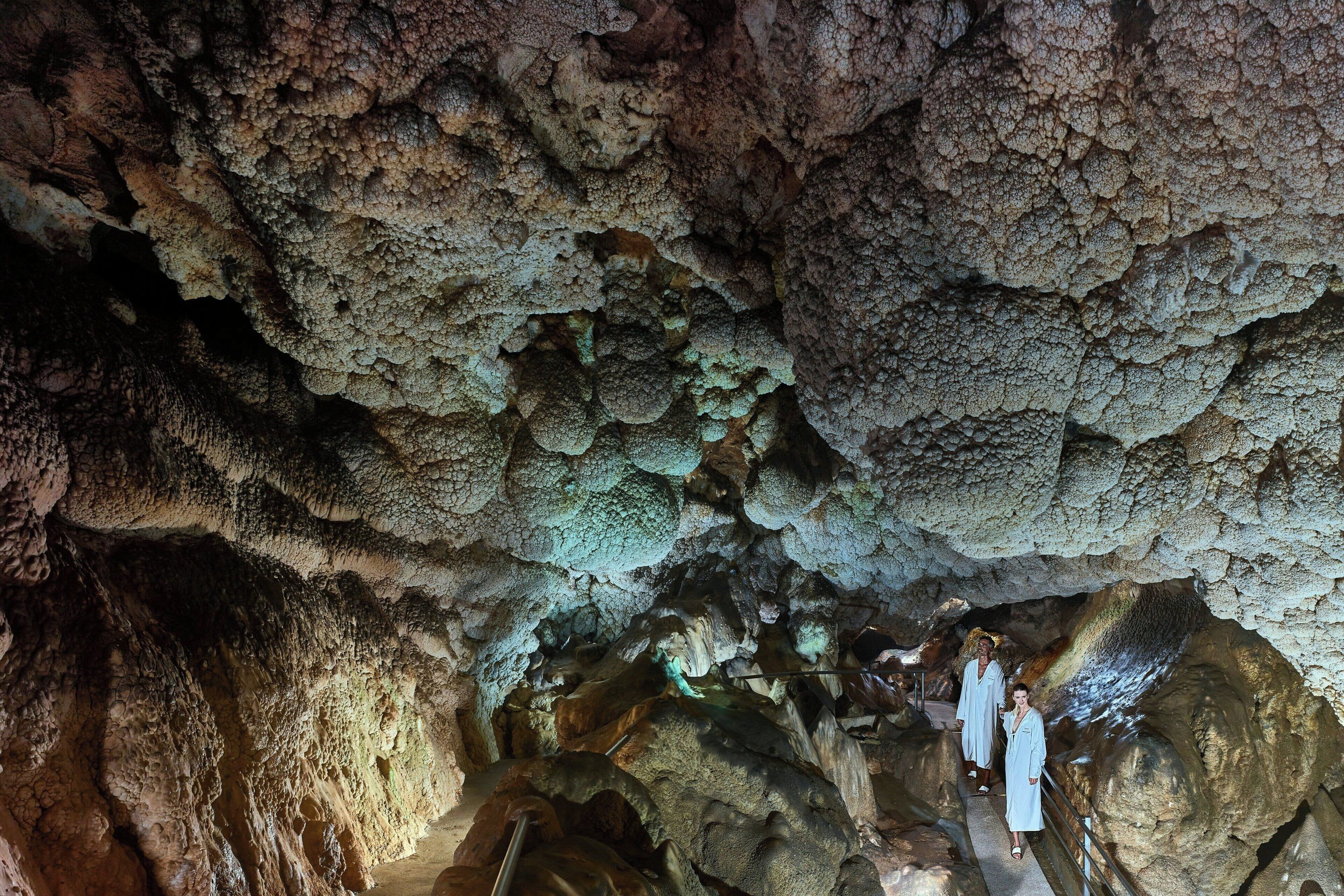 A cave interior with stalactites and stalagmites, a pathway, and visitors.
