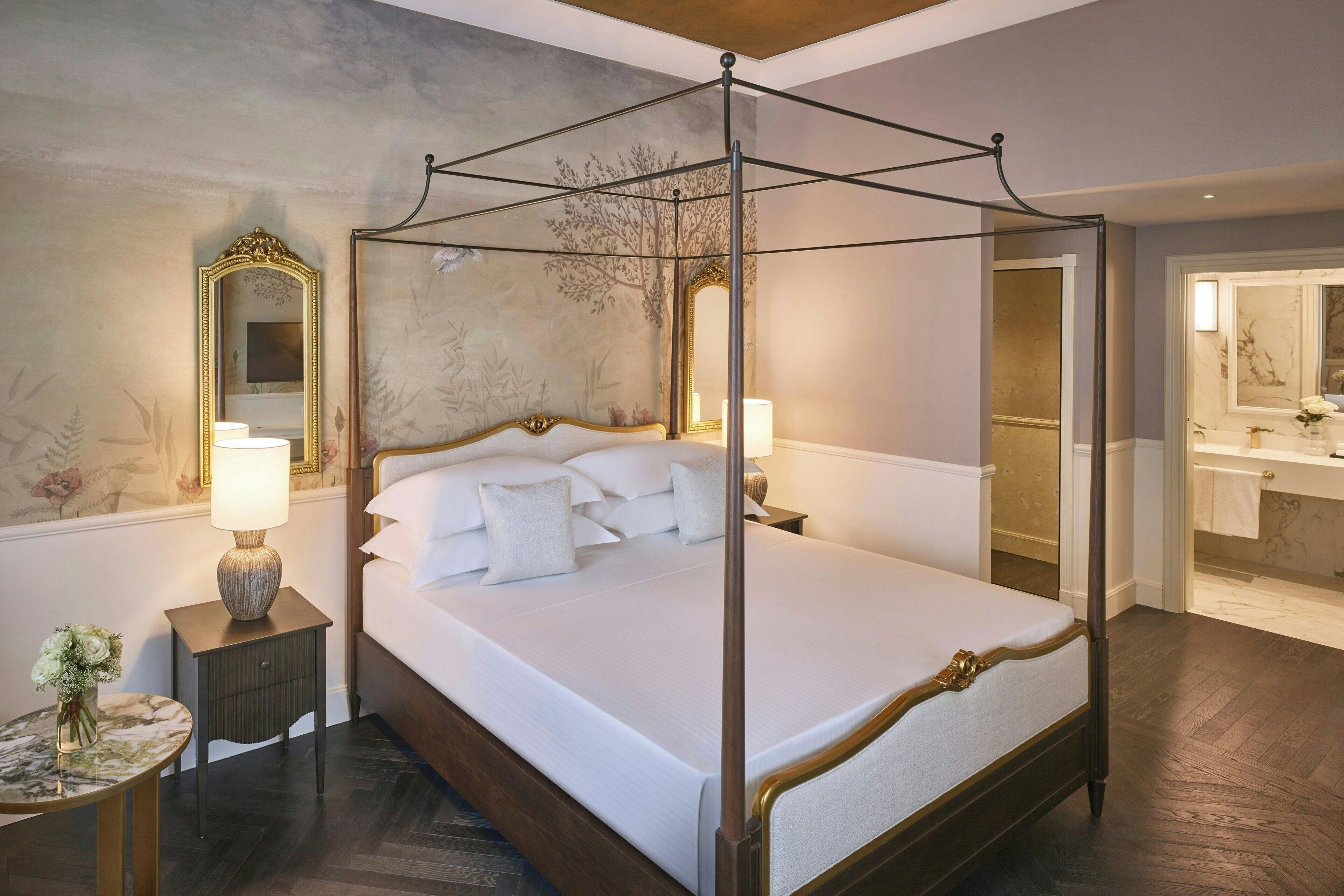 Una cama con dosel con ropa de cama blanca, una mesita de noche con lámpara y un espejo en la pared.