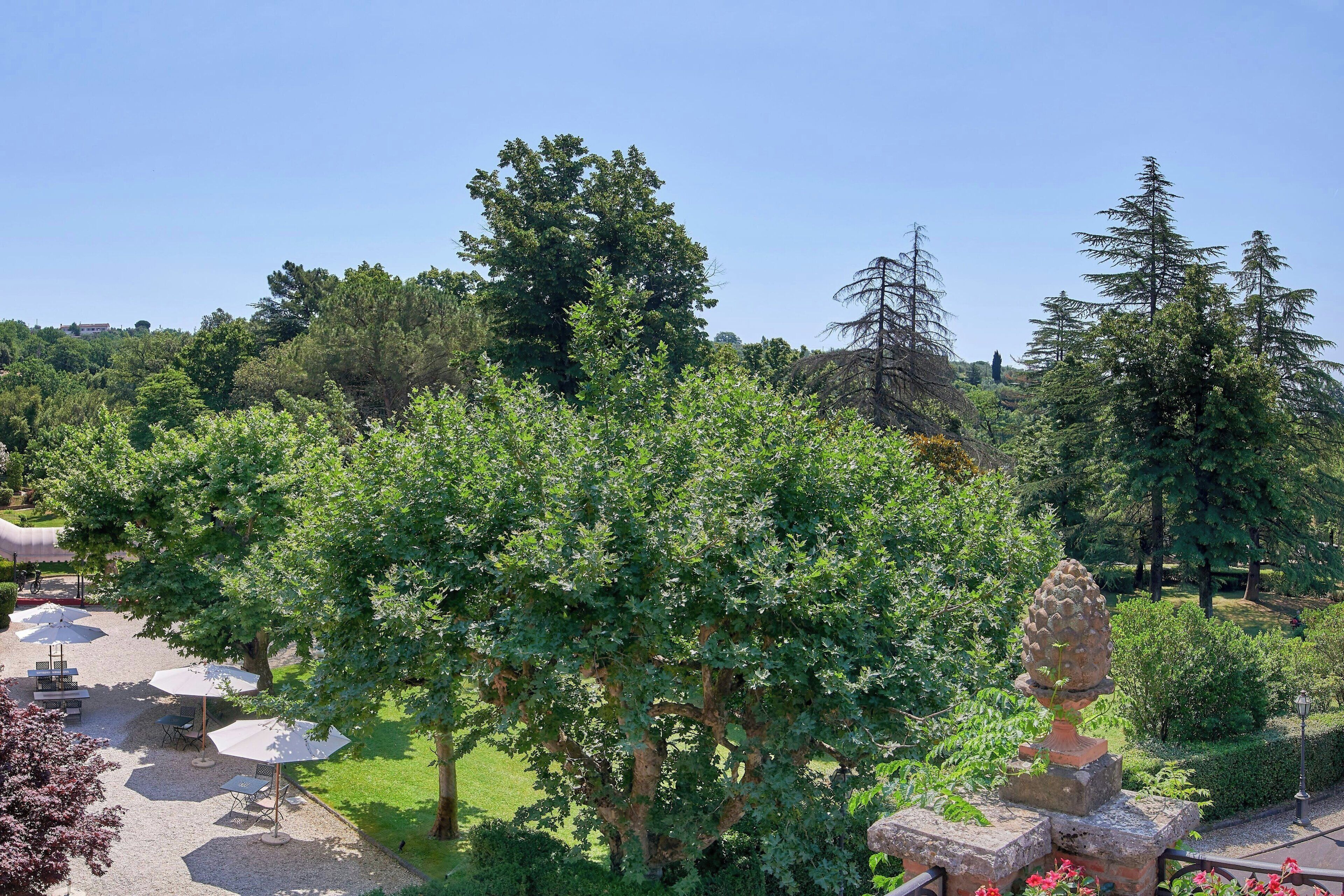 Un espace jardin agrémenté d’arbres, d’une sculpture en pierre et de coins salons extérieurs avec des parasols.