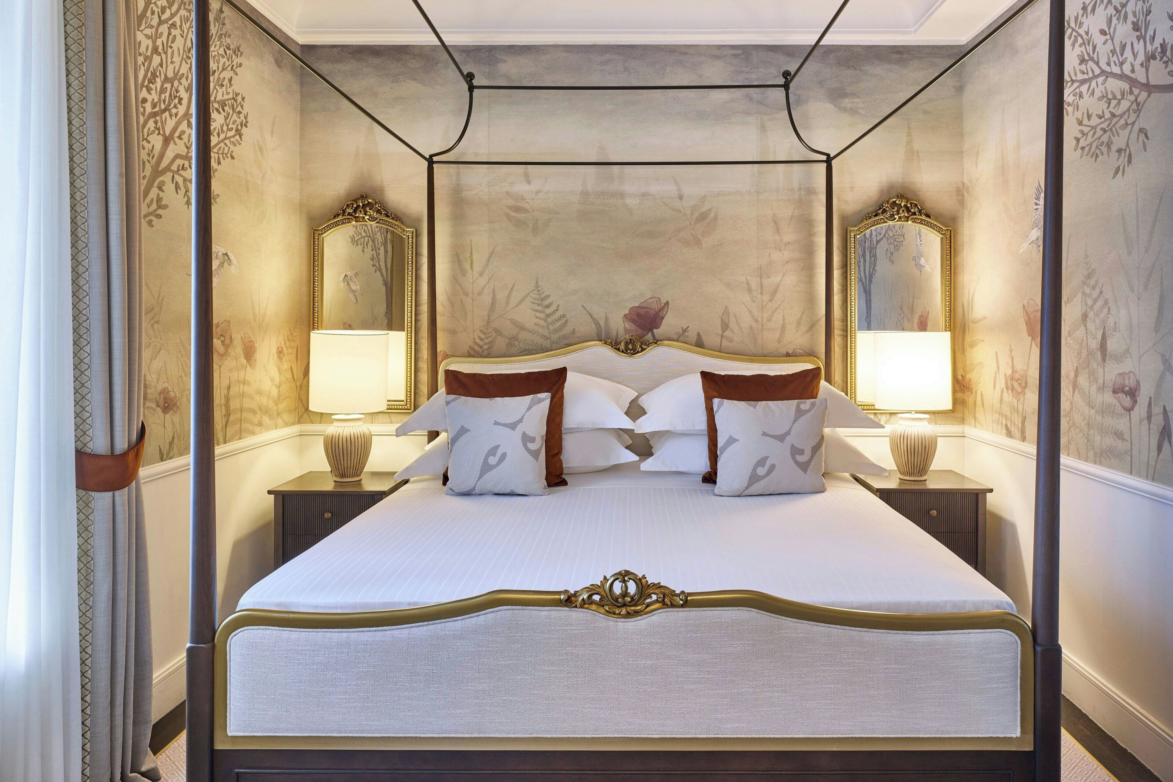 A four-poster bed with a floral headboard, two bedside tables with lamps, and a large mirror on the wall.