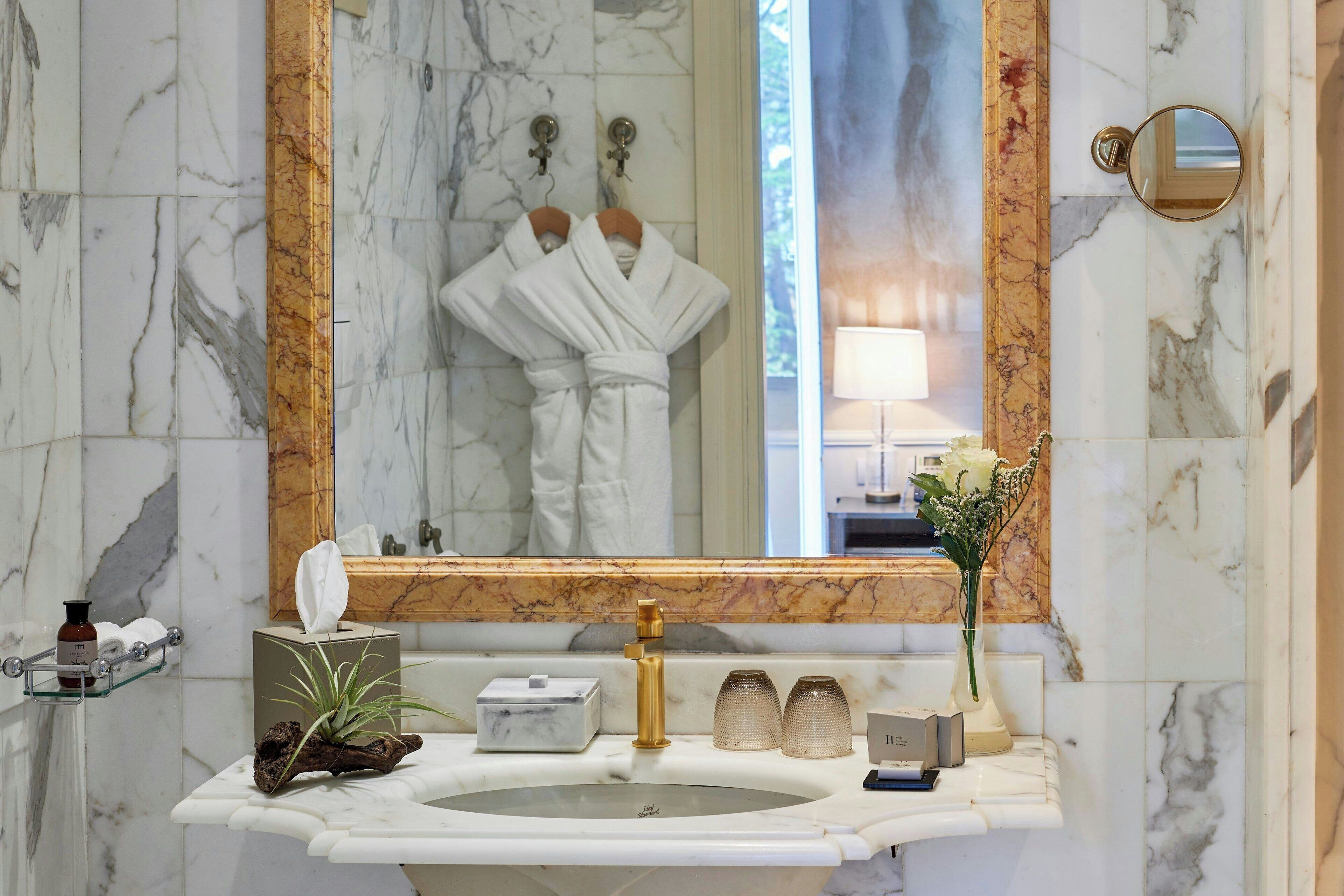 A bathroom with a marble sink, gold fixtures, a mirror, and a vase with flowers.