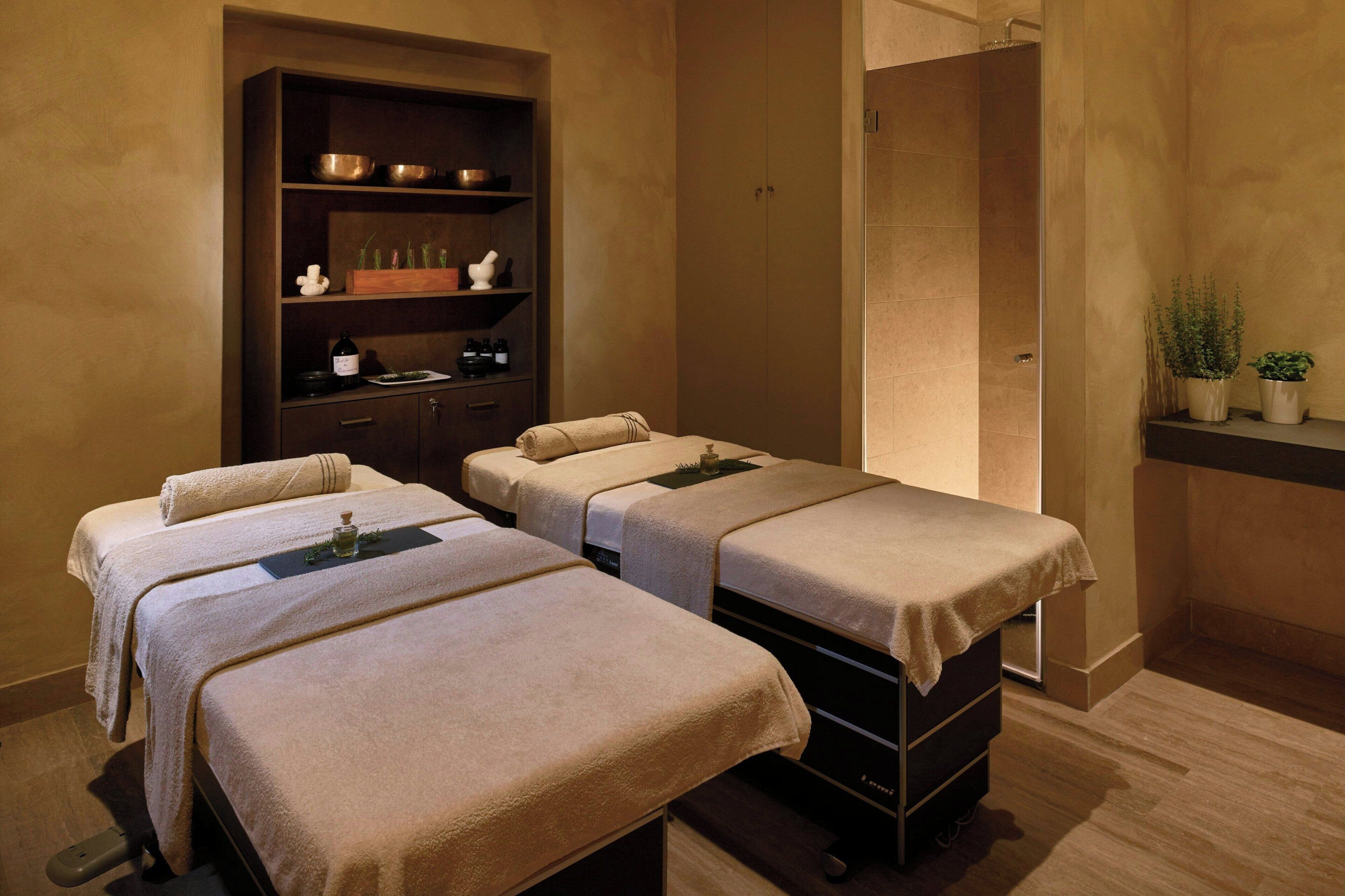 Ein Spa-Raum mit drei Massagetischen, einem Regal mit Flaschen und Schalen sowie einem Duschbereich.