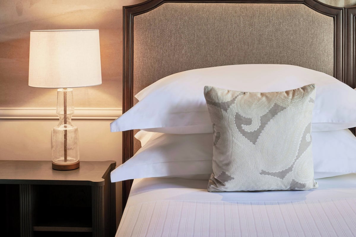 A neatly made bed with a patterned pillow and a bedside lamp on a wooden nightstand.