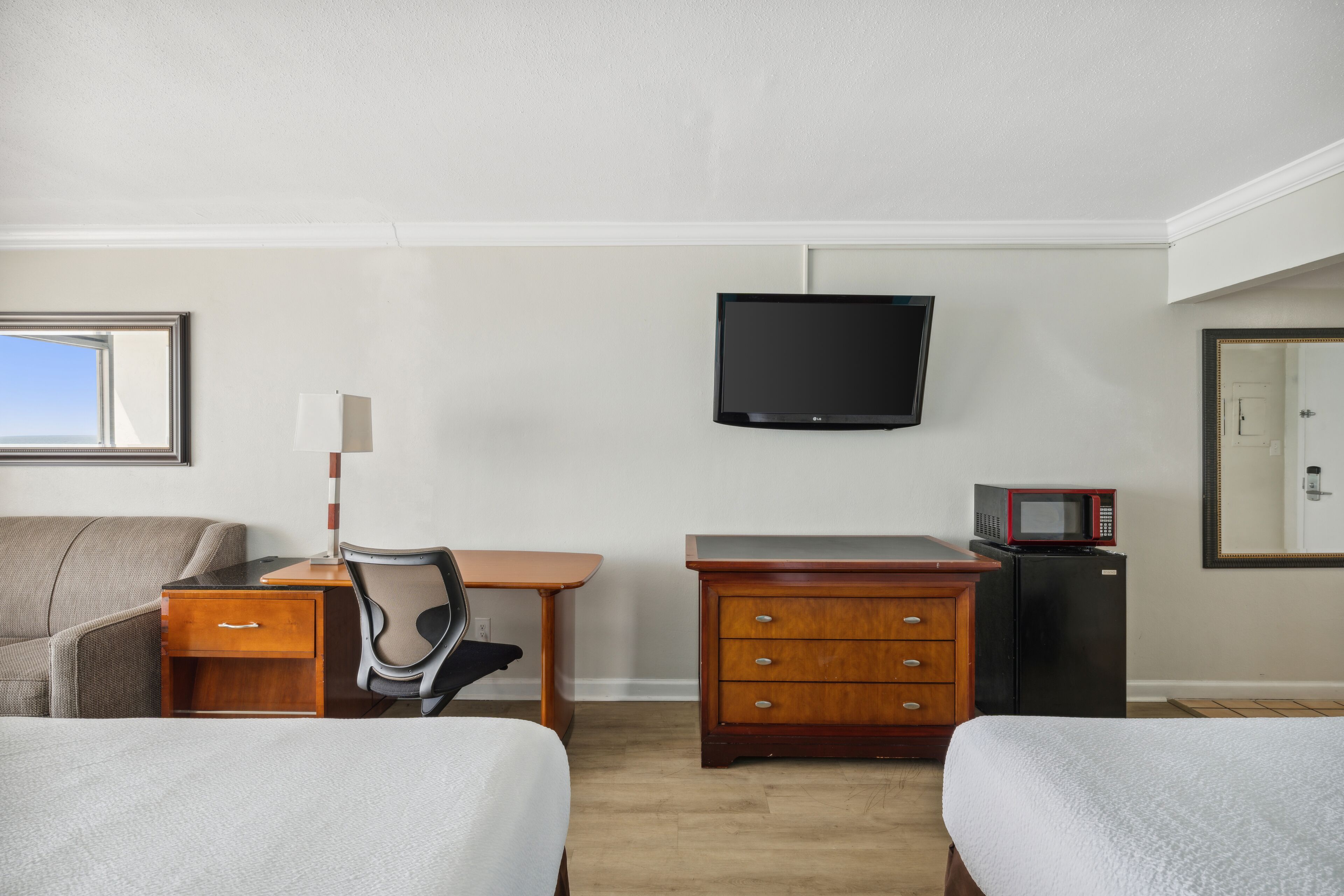 Quarto de hotel com cama, escrivaninha com cadeira, televisão, micro-ondas e cômoda.