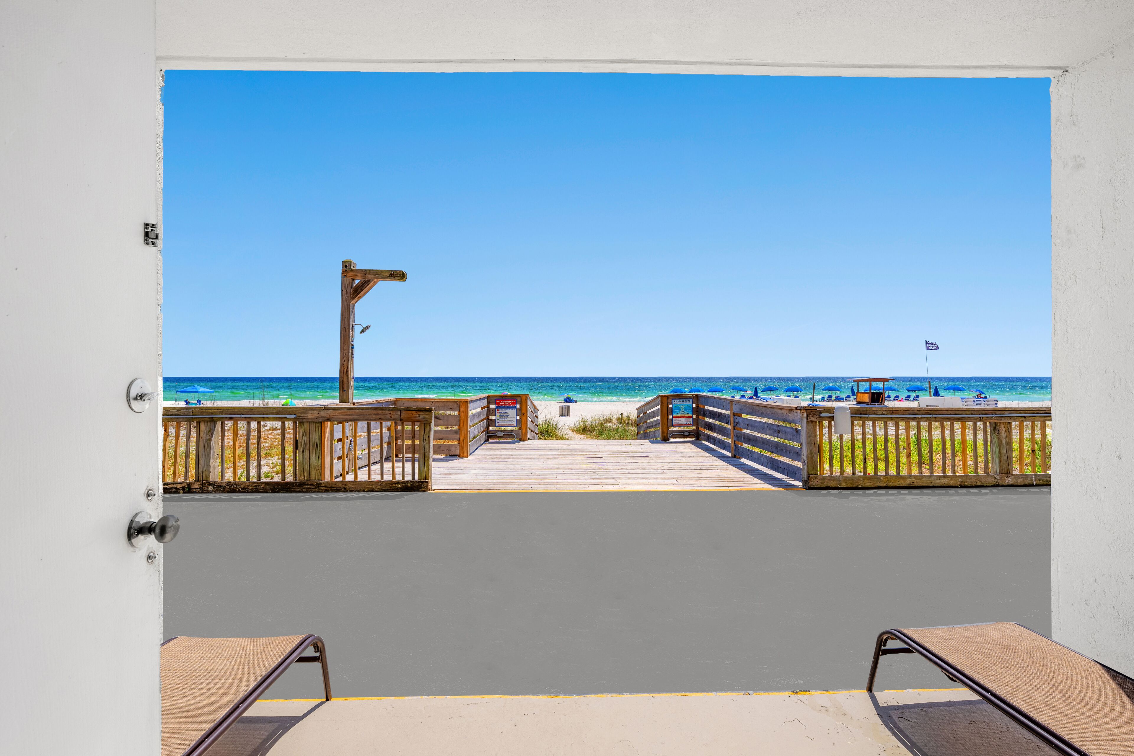 Vista desde un balcón a una playa con un paseo de madera y barandillas.