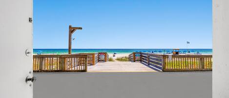 A view from a balcony to a beach with a wooden walkway and railings.