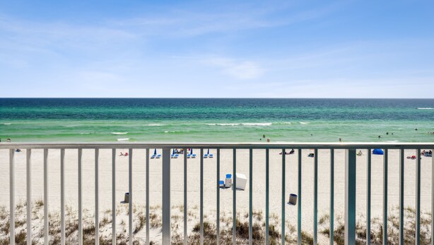 Uma praia com vista clara do oceano, areia e um corrimão em primeiro plano.