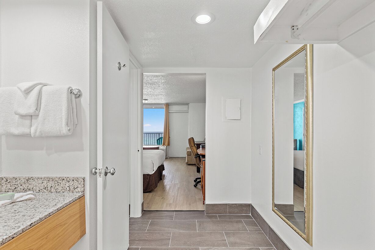 A hotel room with a bathroom, a dining area, and a view of the sea.