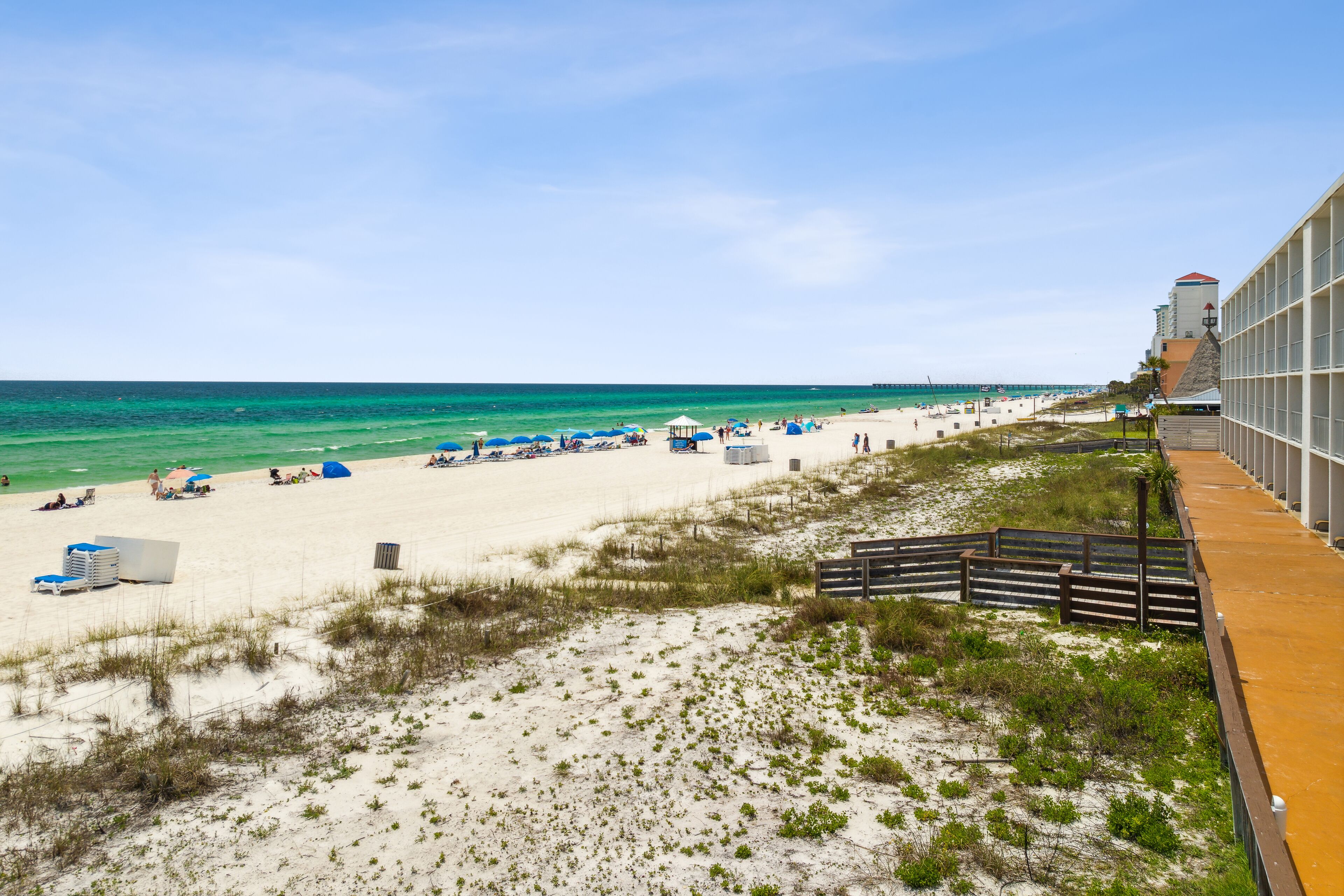 A beach with a long boardwalk, beach umbrellas, and a building with a red roof.
