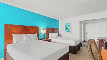 Une chambre d’hôtel avec deux lits, une tête de lit en bois, un mur d’accent de couleur turquoise, un tableau, un bureau et une chaise.