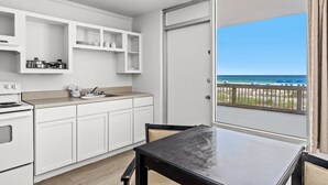 Cozinha com armários brancos, bancada preta e vista para a praia através de uma porta de correr.