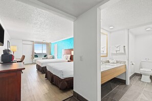 A hotel room with two beds, a desk, a TV, a bathroom with a toilet and sink.