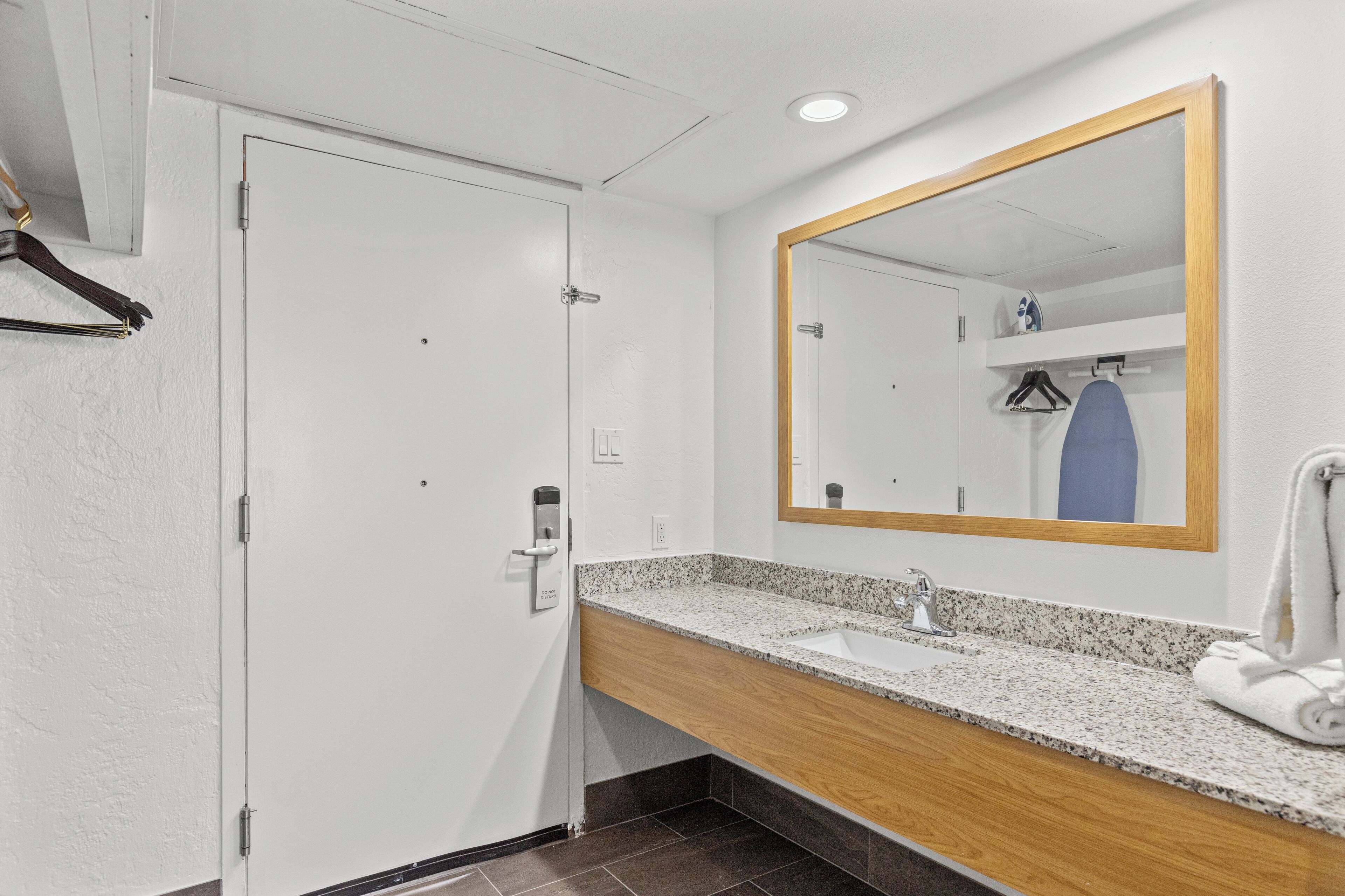 A bathroom with a white door, a wooden vanity, a sink, a mirror, and a towel.