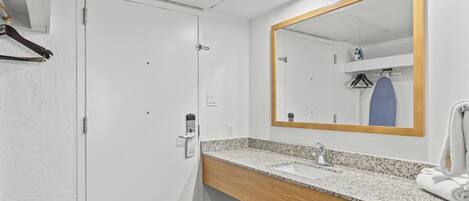 Un baño con una puerta blanca, un tocador de madera, un lavabo, un espejo y una toalla.