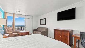 A hotel room with a large bed, a desk, a chair, a dresser, and a TV on the wall.