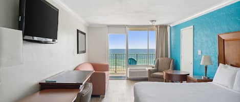 Habitación de hotel con cama, escritorio, silla, televisor y balcón con vista al océano.
