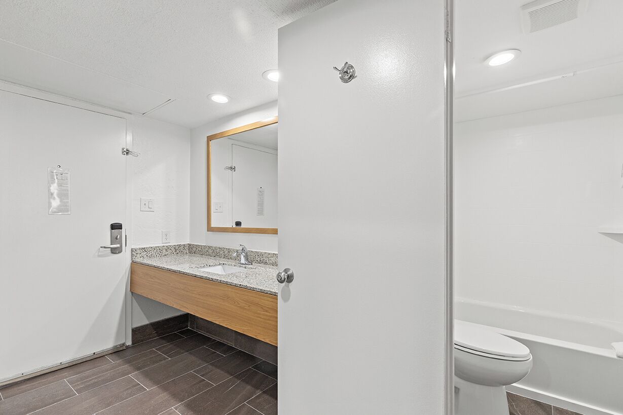 Une salle de bain moderne avec un meuble-lavabo en bois, un grand miroir, des toilettes et une baignoire.