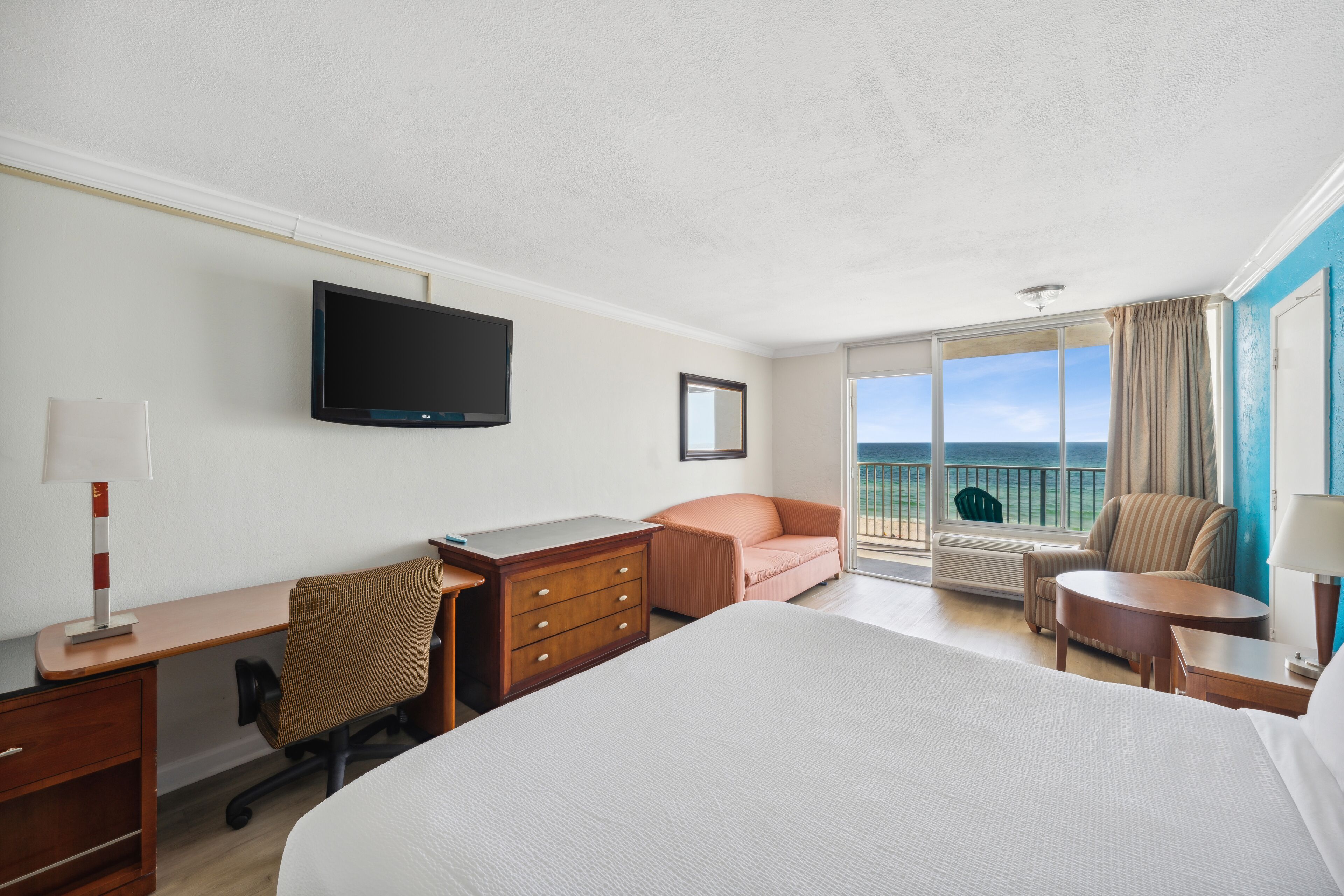 Ein Hotelzimmer mit einem großen Bett, einem Schreibtisch, einem Sessel, einem Fernseher und Meerblick.