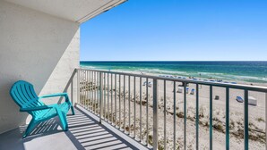 Uma varanda com uma cadeira Adirondack azul-turquesa, vista para a praia e um corrimão.