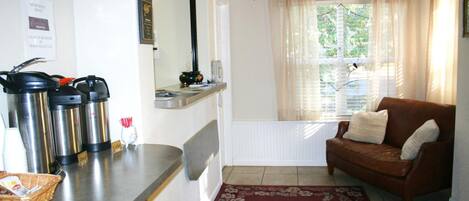 A cozy living room with a brown leather sofa, a coffee station with thermos cups, and a window with sheer curtains.