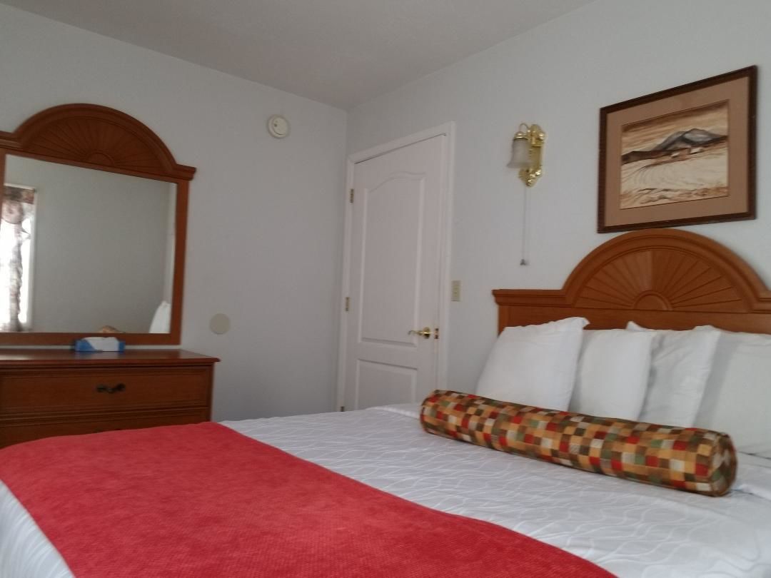 Une chambre d’hôtel comprenant un lit, une commode, un miroir, une porte et un luminaire fixé au mur.