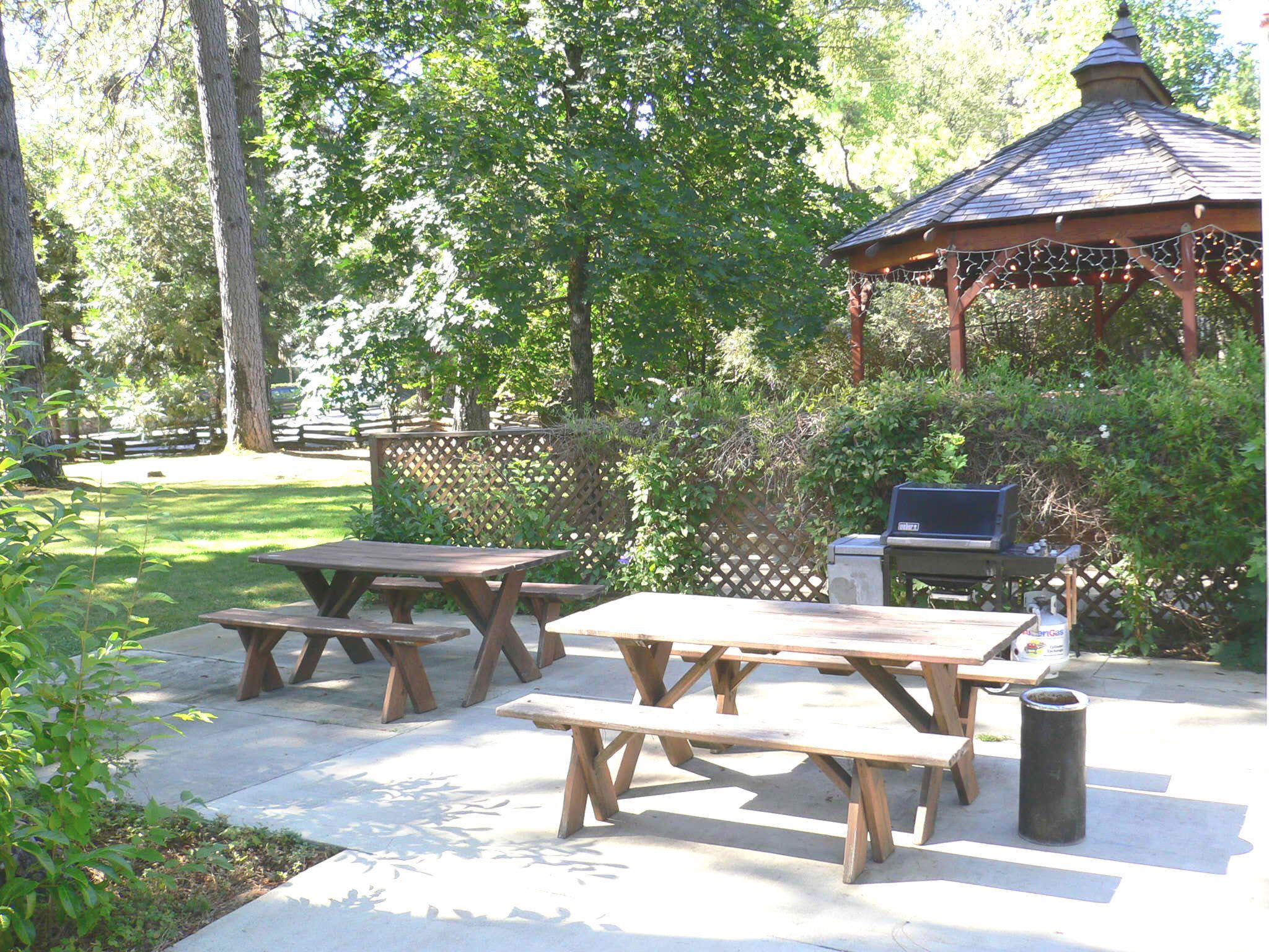 Un patio al aire libre con mesas de picnic y una parrilla.