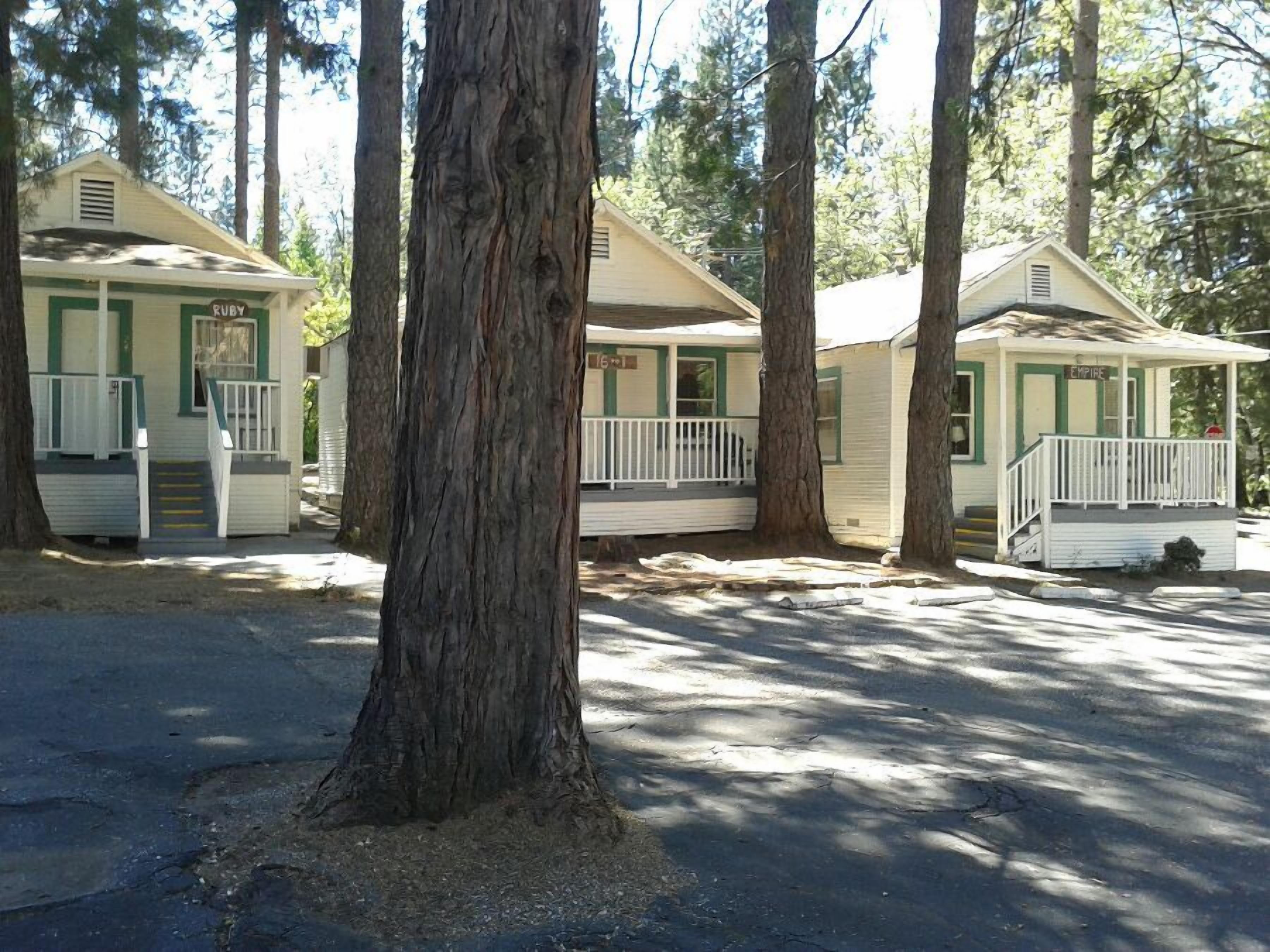 A row of cabins with green trim and white exteriors, each with a porch and steps leading to the entrance.