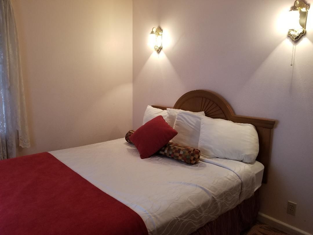 A neatly made bed with white and red bedding, two wall-mounted light fixtures, and a wooden headboard.