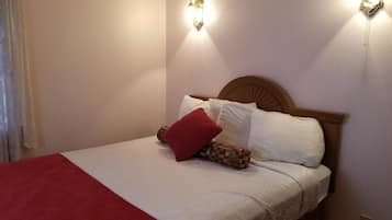 A neatly made bed with white and red bedding, two wall-mounted light fixtures, and a wooden headboard.