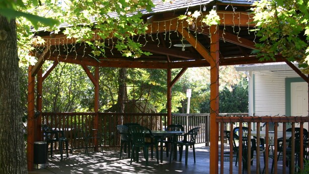 A covered outdoor seating area with tables and chairs, surrounded by trees and a house in the background. - Nevada City Inn (Nevada City)