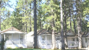 A row of white mobile homes with porches, surrounded by tall trees. - Nevada City Inn (Nevada City)