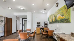 Un espace repas moderne avec un plancher en bois, des chaises orange, un comptoir en granit et un grand tableau abstrait accroché au mur.
