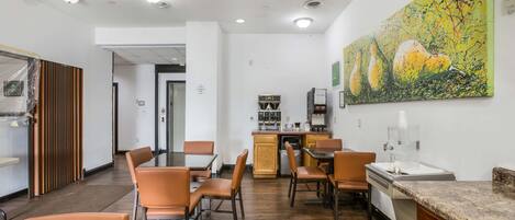 Un espace repas moderne avec un plancher en bois, des chaises orange, un comptoir en granit et un grand tableau abstrait accroché au mur.