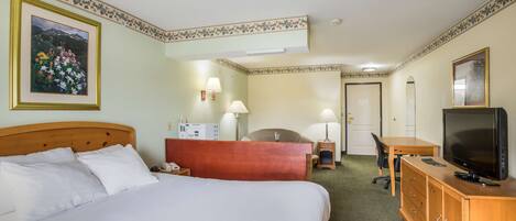 A hotel room with a large bed, a desk, a television, and a chair.
