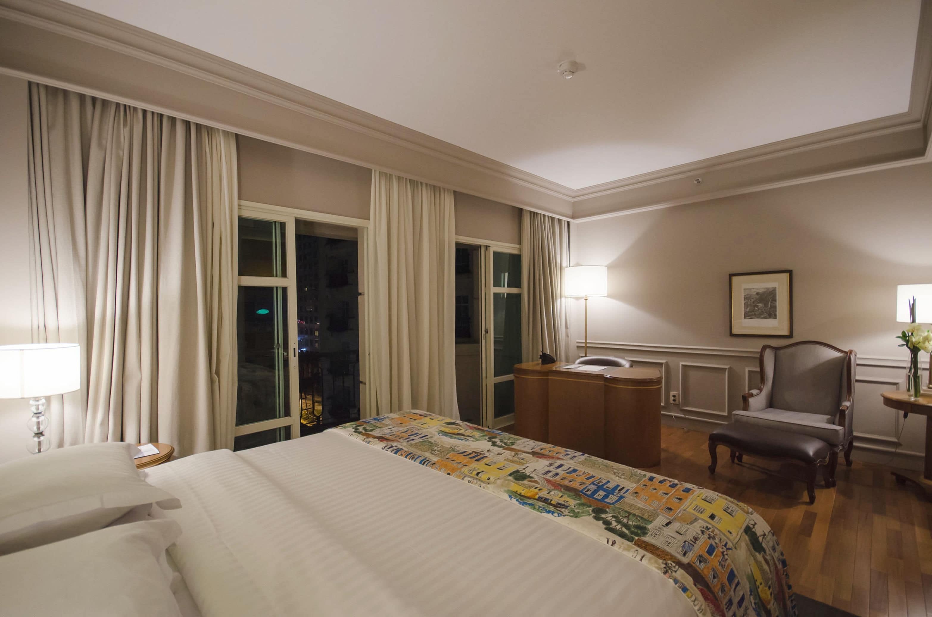 A hotel room with a large bed, a desk, a chair, and a window with curtains.