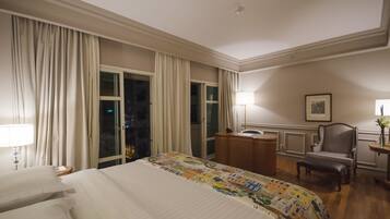 Una habitación de hotel con una cama grande, un escritorio, una silla y un ventanal con cortinas.