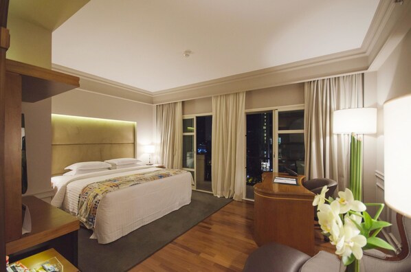 A hotel room with a large bed, a desk, a chair, and a view of the city at night. - Gran Estanplaza Berrini (São Paulo)