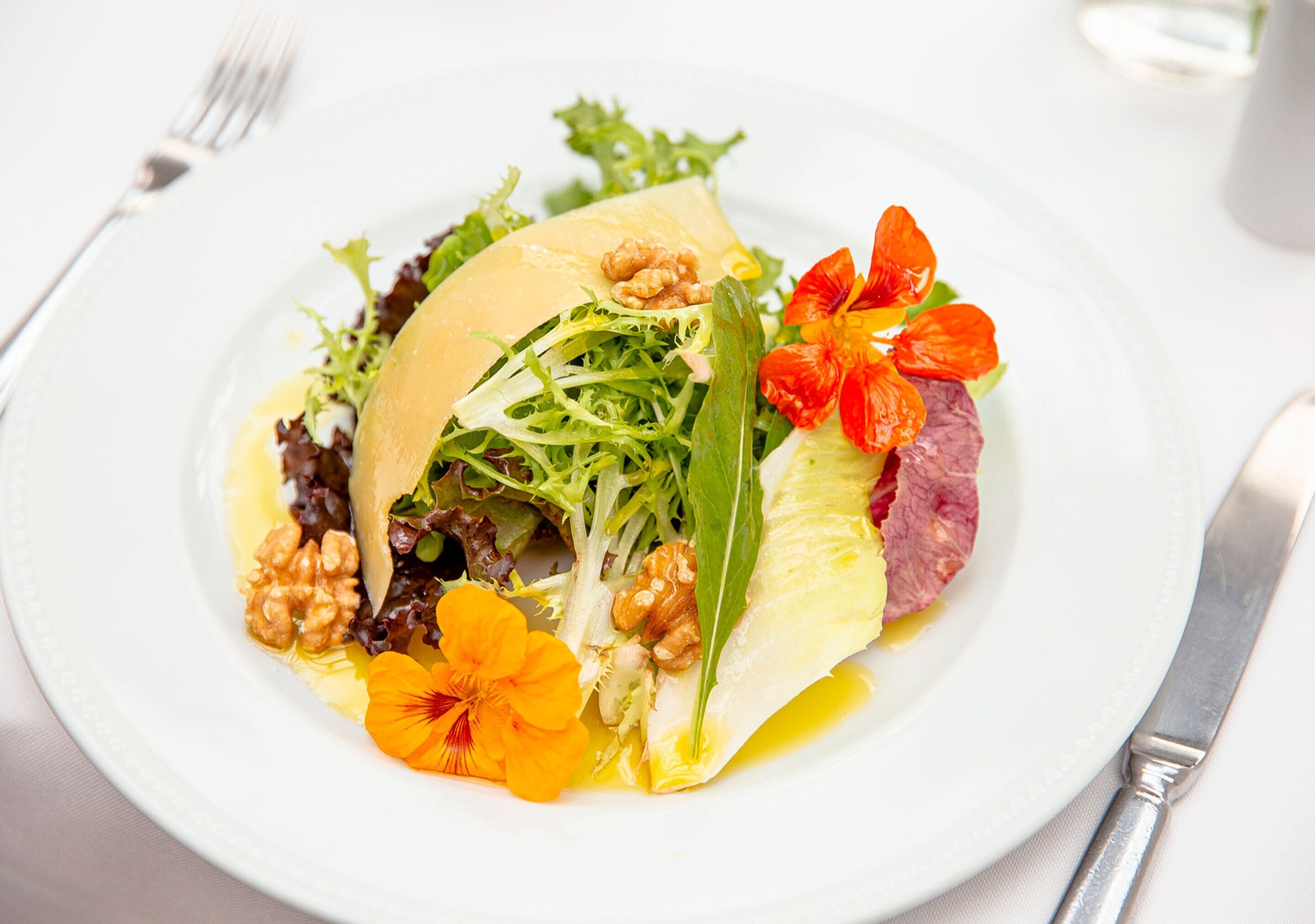 Un plato blanco con ensalada, nueces y flores.