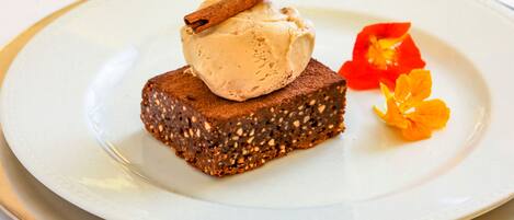 A dessert on a plate with a piece of cake topped with ice cream and a cinnamon stick, accompanied by a small orange flower.