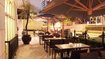 An outdoor cafe with tables and chairs, umbrellas, and a potted plant.