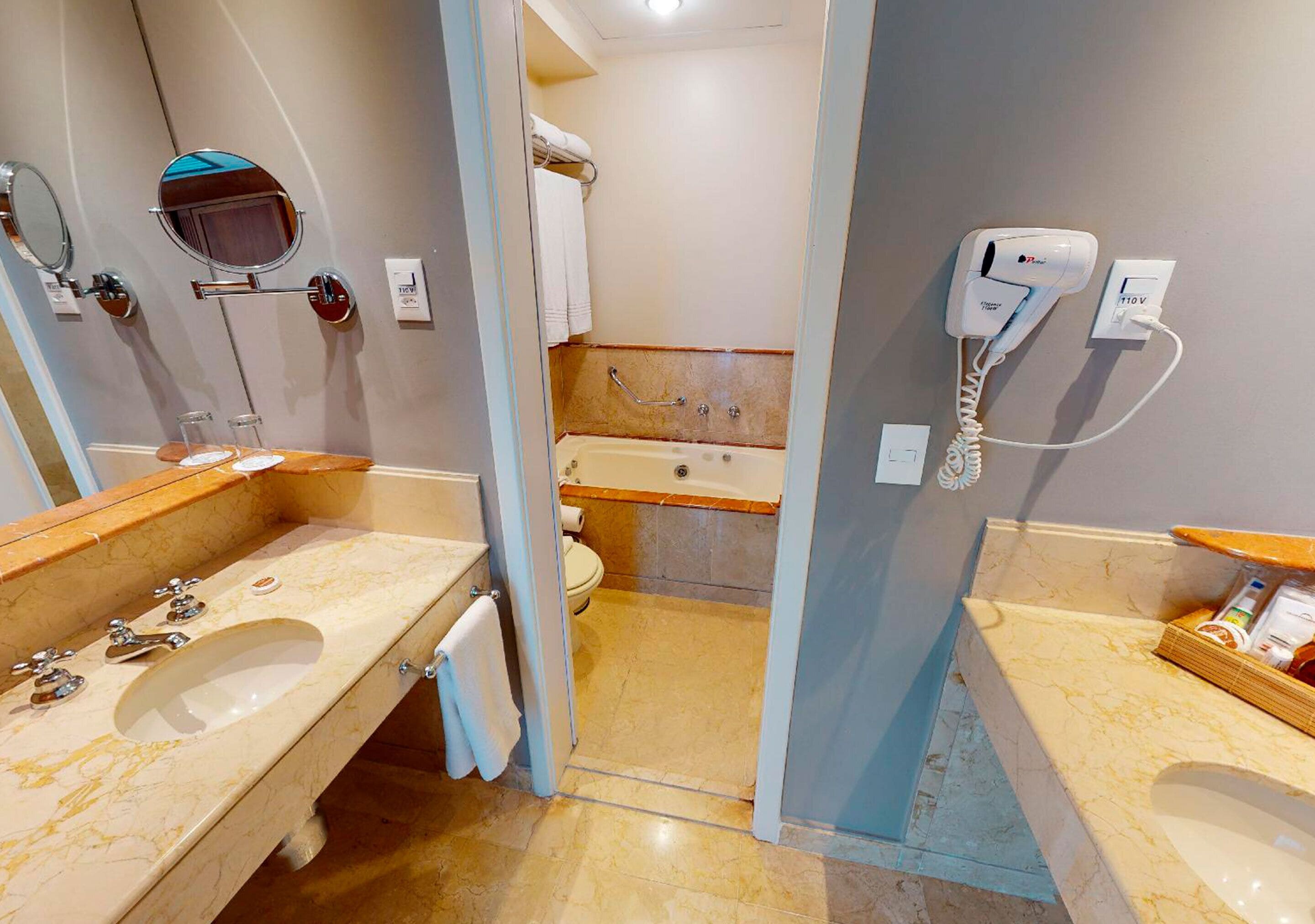 Un baño con lavamanos, espejo, toallero y secador de pelo en la pared.