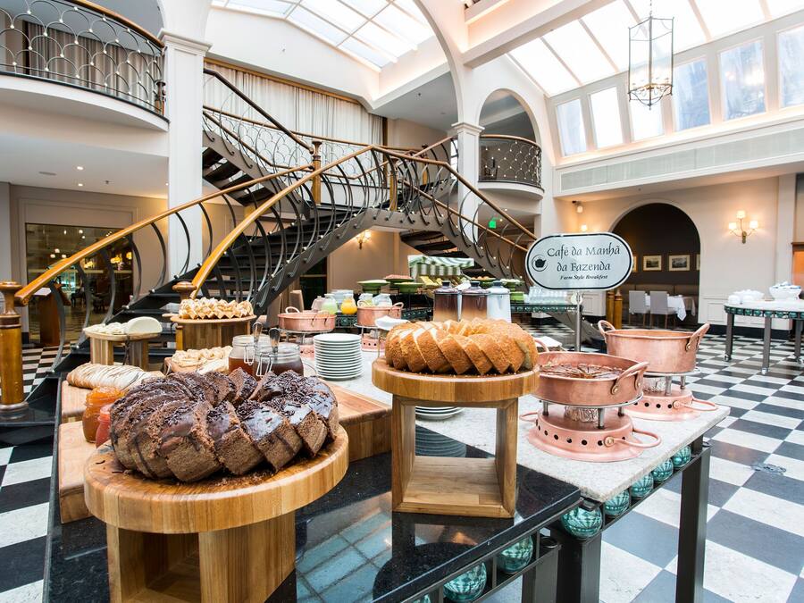A hotel lobby with a checkered floor, a staircase, and a variety of baked goods displayed on tables.