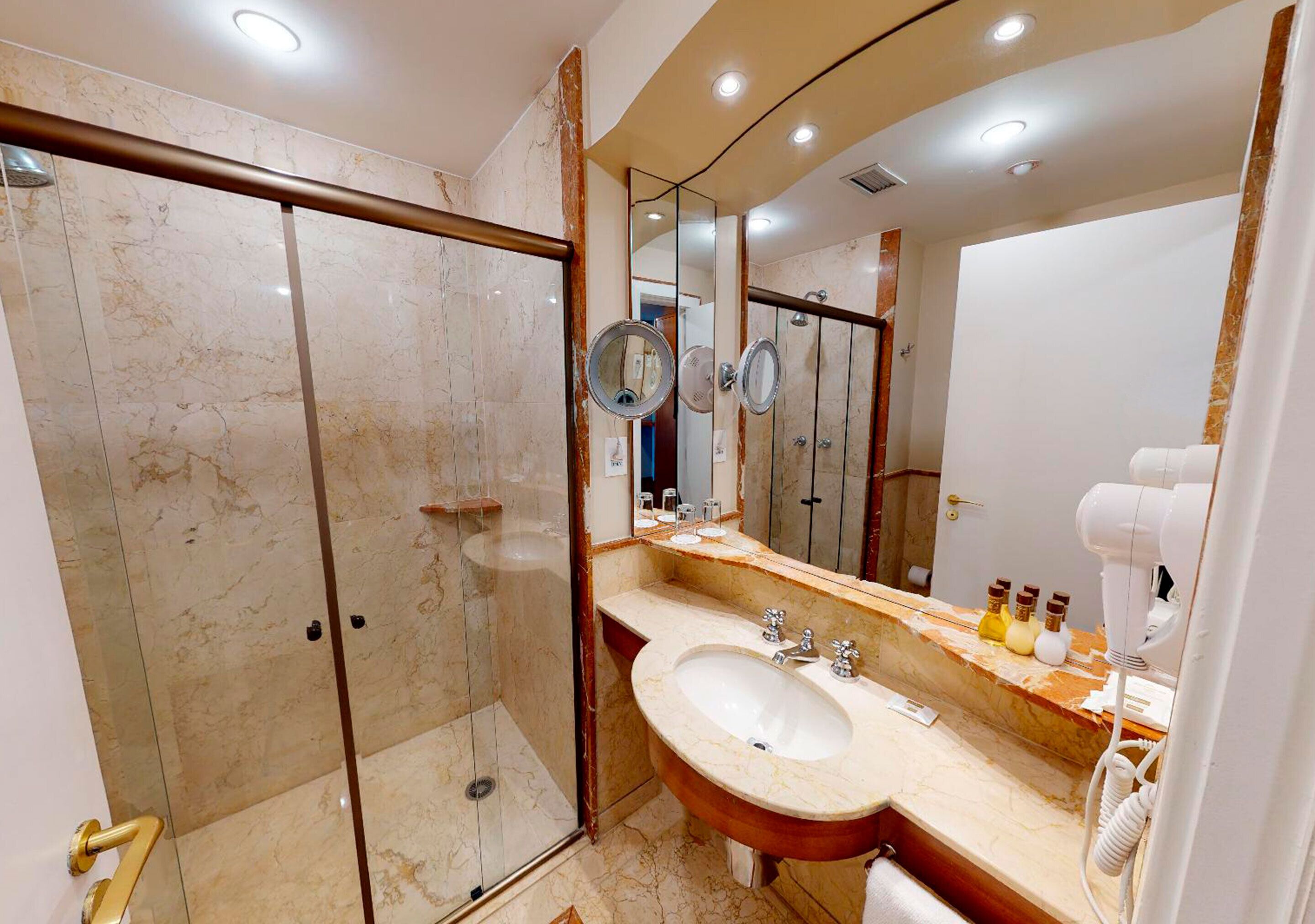 Un baño moderno con tocador de mármol, un espejo grande, secador de pelo de mano y ducha con mampara de vidrio.