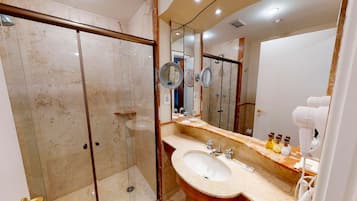 Un baño moderno con tocador de mármol, un espejo grande, secador de pelo de mano y ducha con mampara de vidrio.
