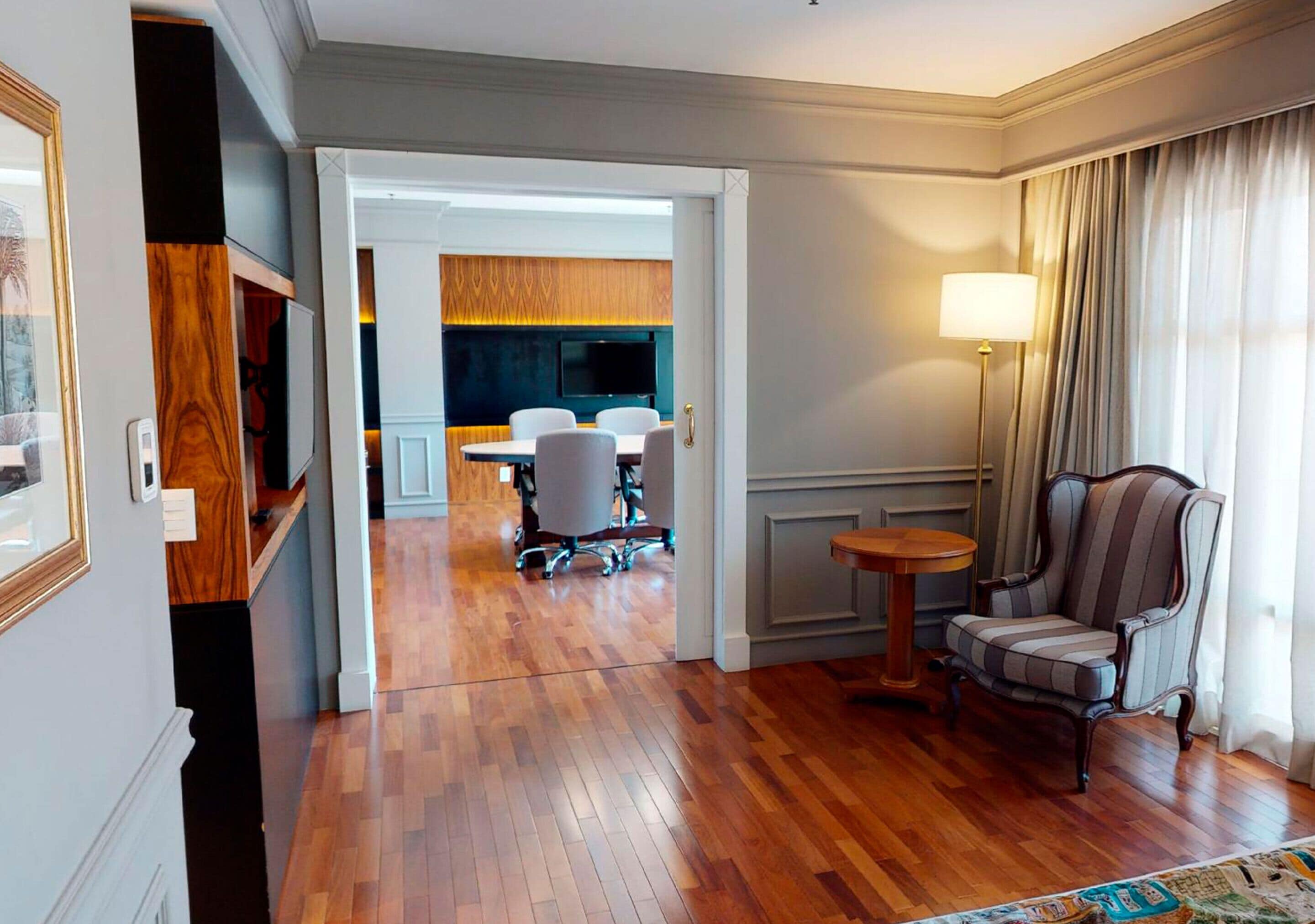 Una habitación de hotel con piso de madera, un área de comedor con una mesa y sillas, una lámpara y un sillón a rayas.