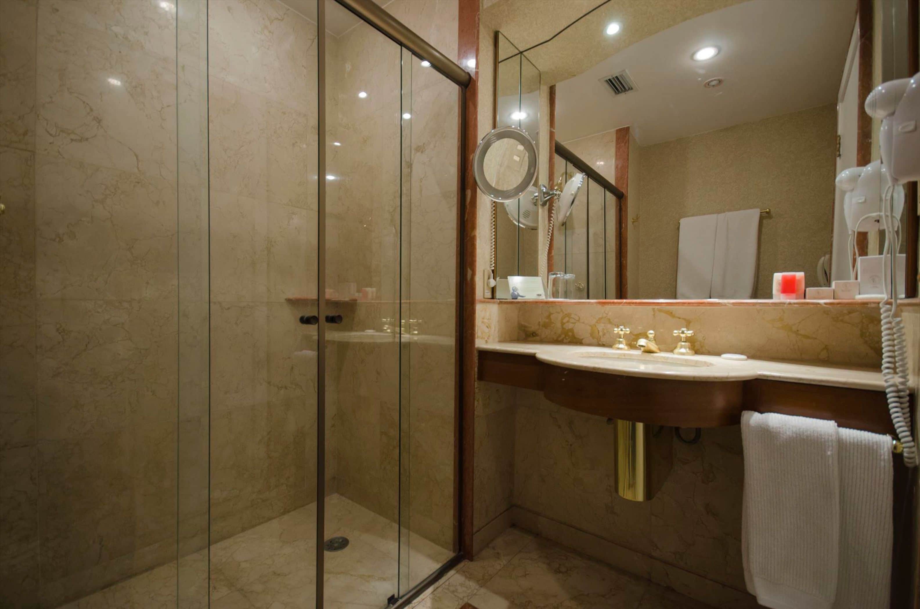 Ein modernes Badezimmer mit einer gläsernen Duschkabine, einer marmorverkleideten Wand, einem Waschtisch und einem großen Spiegel.