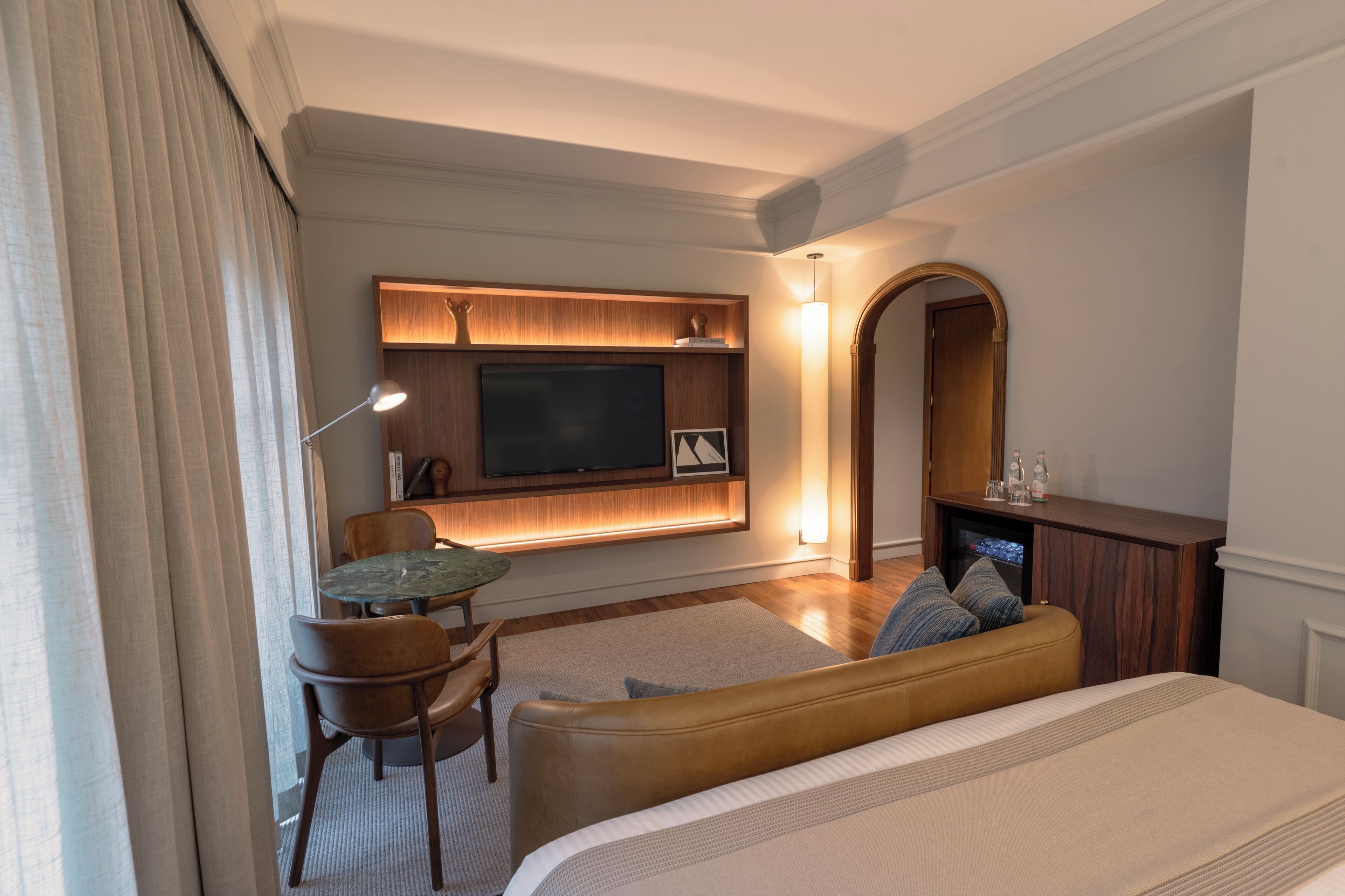 Habitación de hotel con cama, zona de estar con mesa y sillas, televisión de pantalla plana en la pared y chimenea.