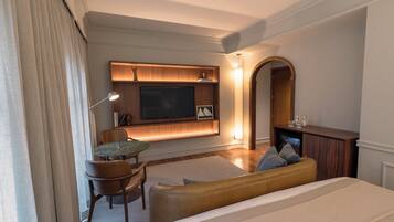 Habitación de hotel con cama, zona de estar con mesa y sillas, televisión de pantalla plana en la pared y chimenea.