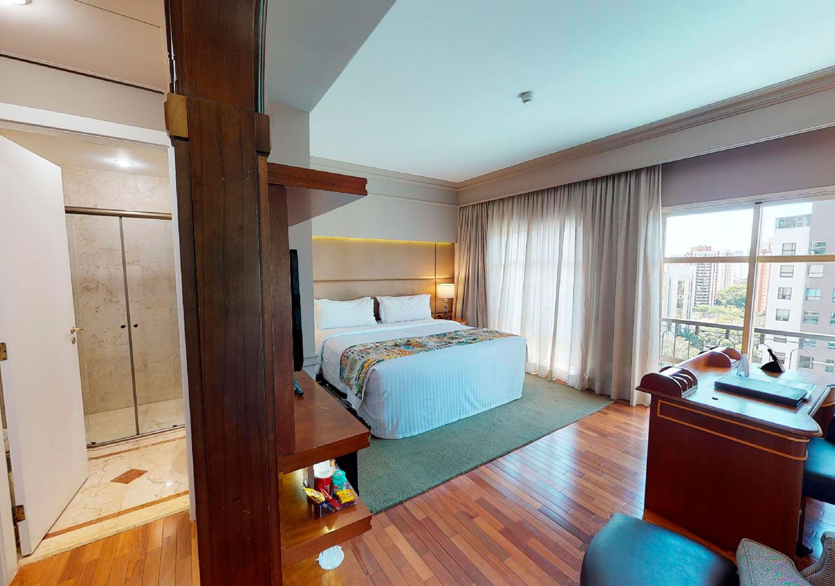Une chambre d’hôtel avec un lit, un bureau, une chaise, une fenêtre avec des rideaux et une vue sur les bâtiments environnants.